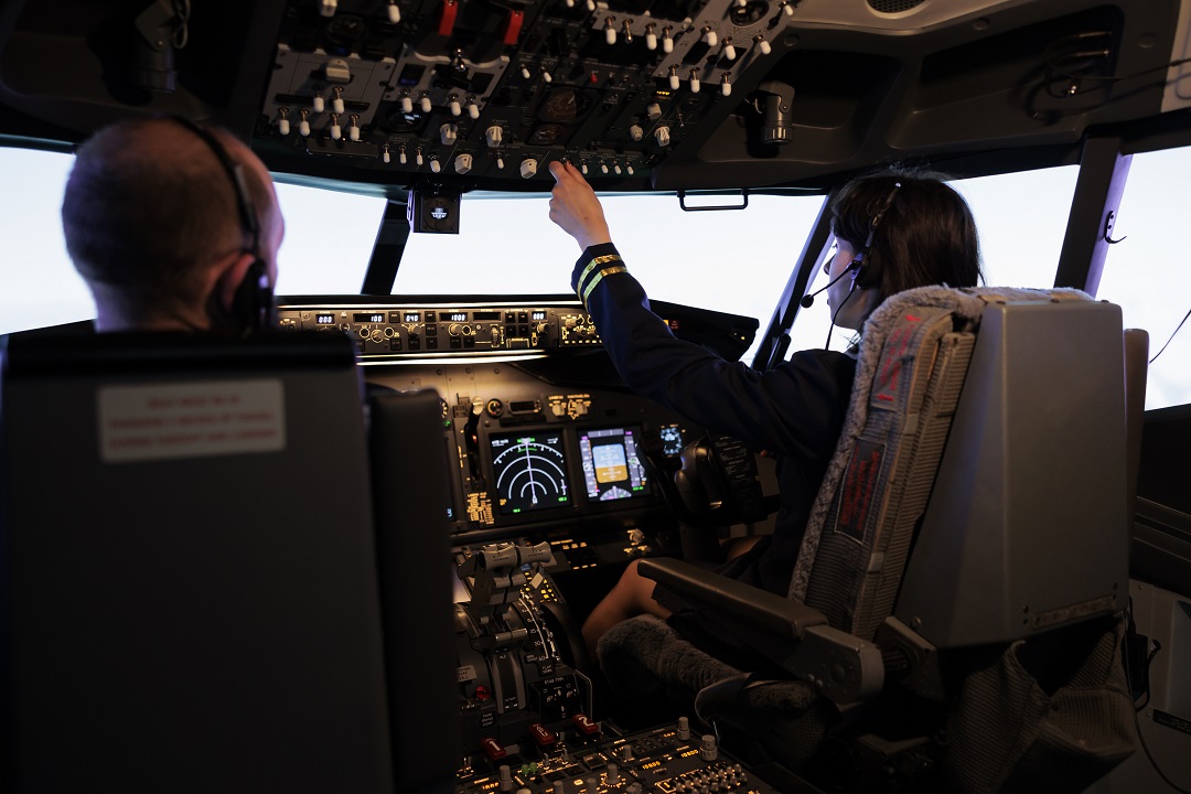 Female pilot assisting captain to takeoff and fly airplane, using buttons on dashboard command in pilot cockpit.