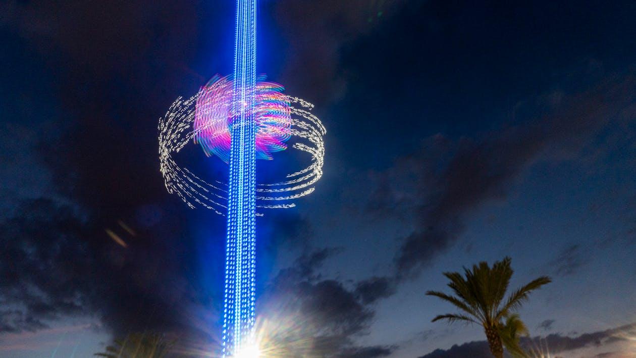 Long exposure of a colorful light tower against a night sky with palm trees below. Captured in Orlando, FL.