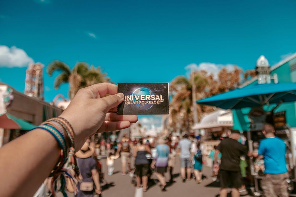 A hand holding a Universal Orlando Resort ticket in a bustling theme park setting.