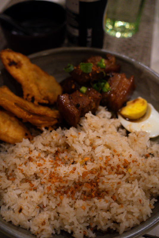 Plate of white rice with fried plantain chips, braised pork chunks with green onions, and a halved hard-boiled egg on the side.