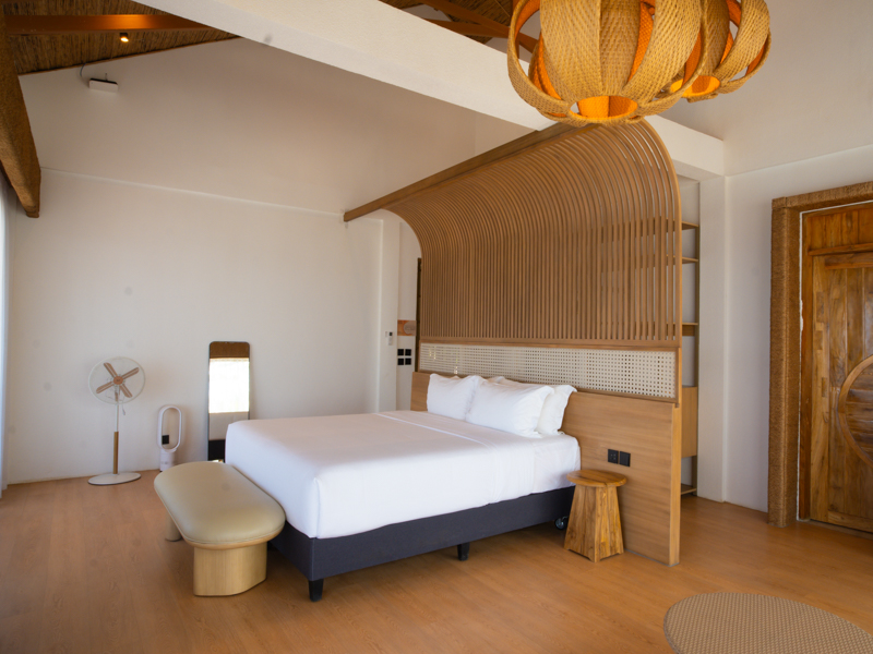 Bedroom with a white bed and curved wooden screen headboard, bench at foot, and warm wood accents
