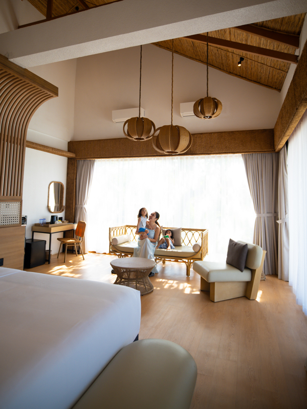 Spacious hotel living area with a family of four by a woven sofa under large pendant lights.