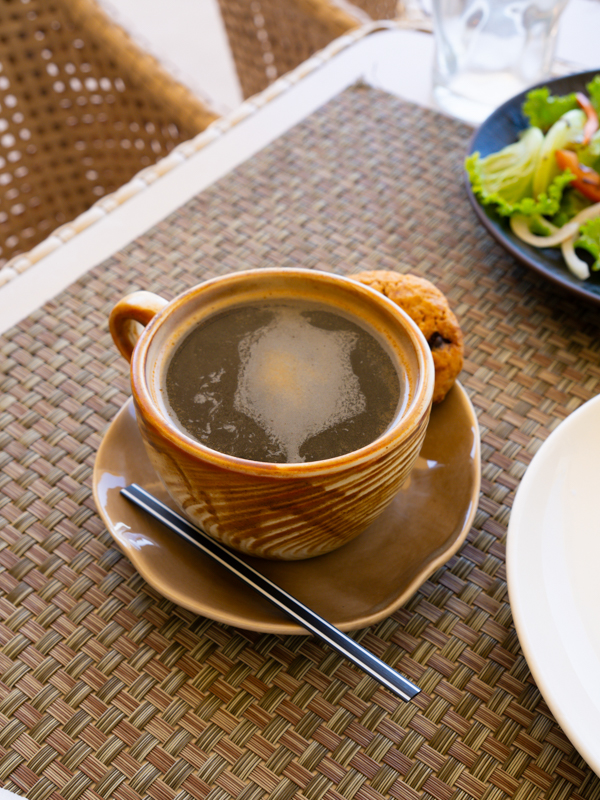 Brown ceramic coffee cup on a matching saucer with a cookie, set on a woven placemat.