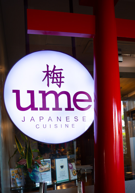 Round illuminated sign for a Japanese restaurant displaying 'ume' with a kanji character above and 'JAPANESE CUISINE' below.